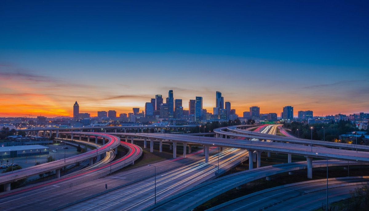 Multi-level freeway interchange at dusk with traffic light trails and a city skyline