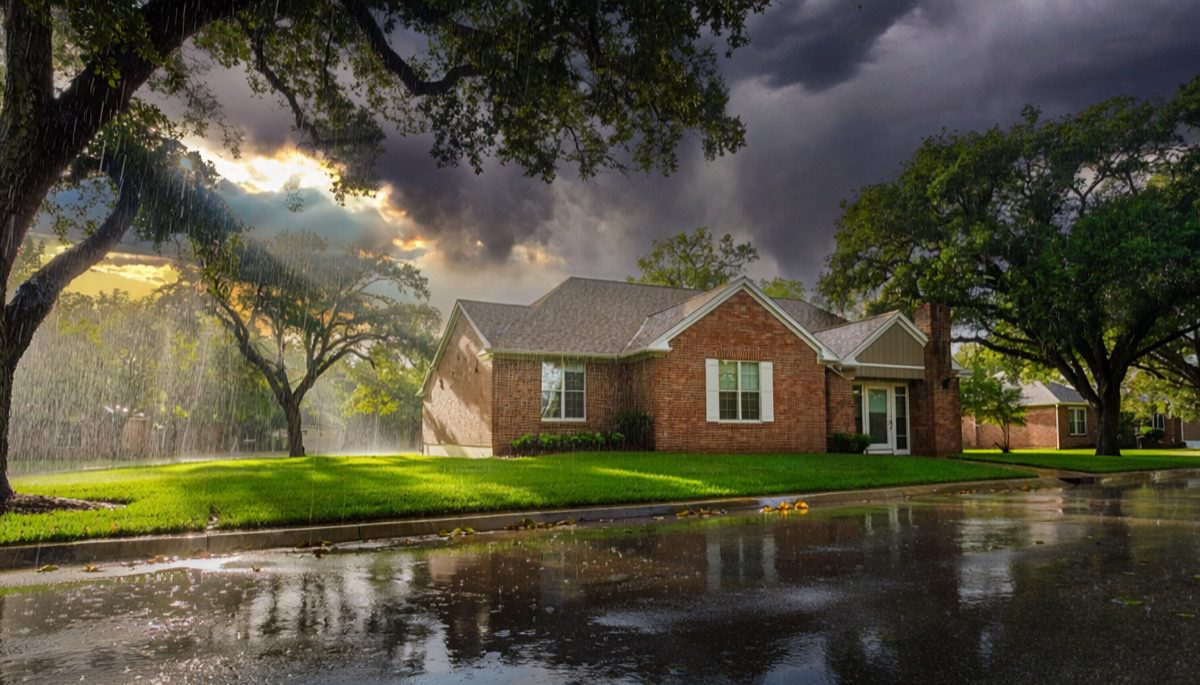 Brick home on a tree-lined street after a summer storm, sun breaking through clearing clouds